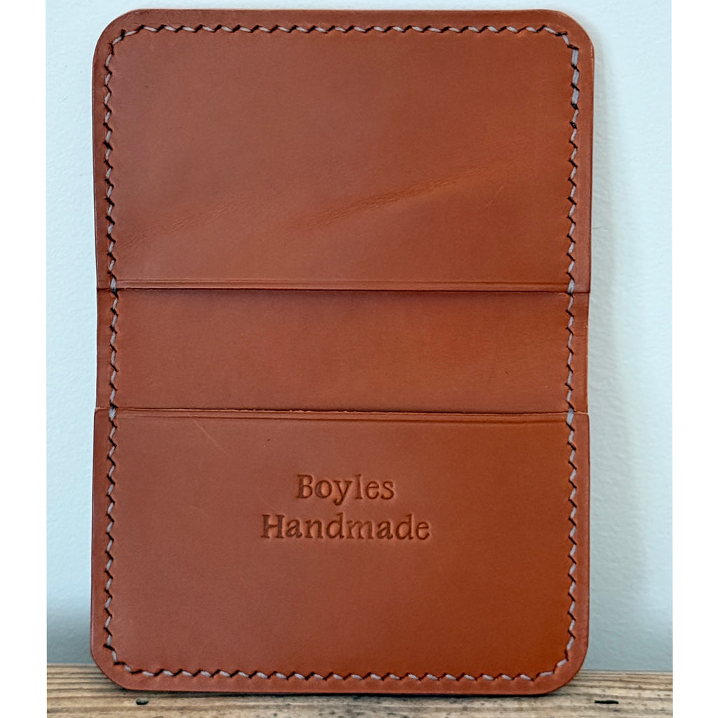 A brown leather card holder or wallet with visible stitching and the embossed text 'Boyles Handmade' on the front, photographed against a light blue wall.